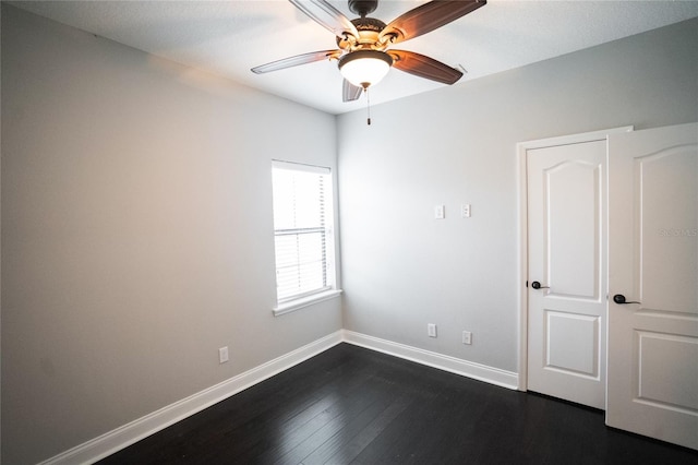 spare room featuring dark wood-style floors, a ceiling fan, and baseboards