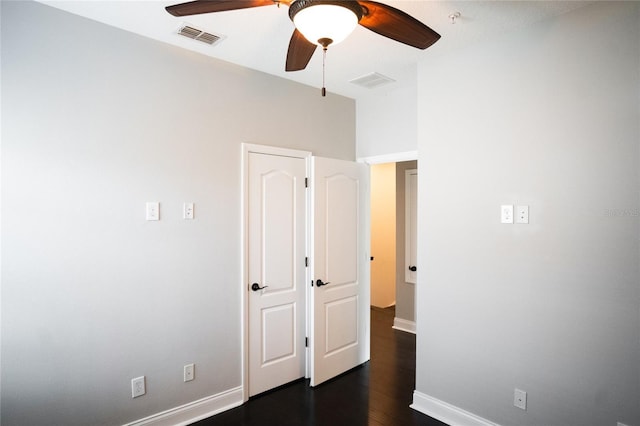 empty room with dark wood-style floors, visible vents, ceiling fan, and baseboards