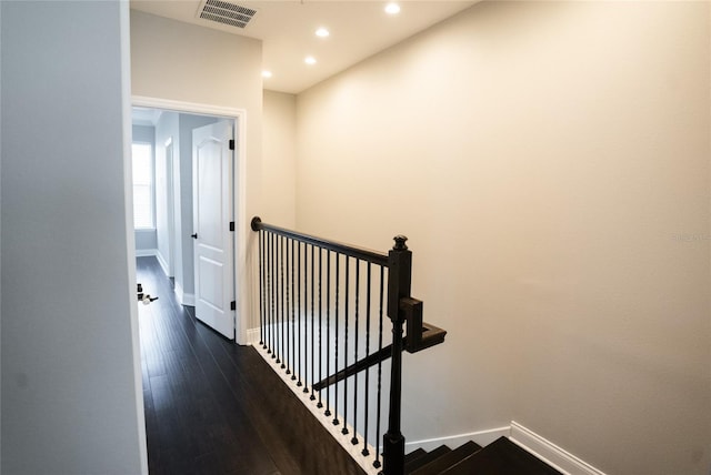 hall featuring dark wood-style flooring, an upstairs landing, visible vents, and baseboards