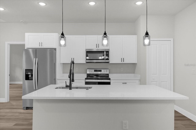 kitchen with stainless steel appliances, a sink, white cabinetry, light countertops, and a center island with sink