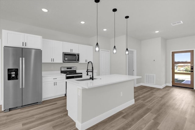 kitchen with stainless steel appliances, visible vents, a sink, and an island with sink