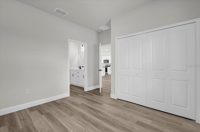 unfurnished bedroom with visible vents, baseboards, a closet, light wood finished floors, and ensuite bath