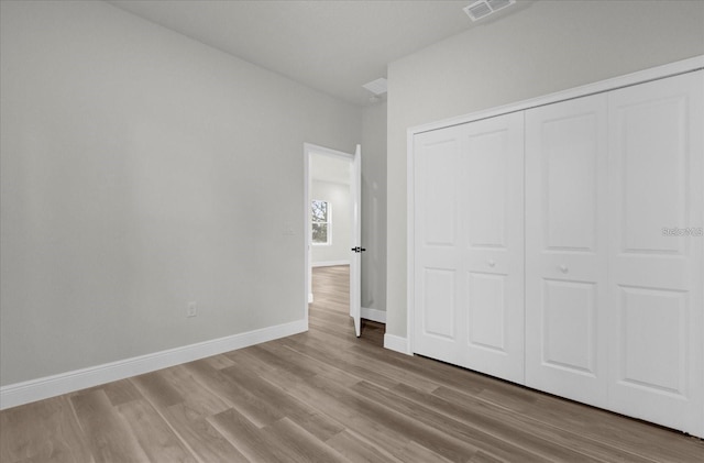 unfurnished bedroom with baseboards, a closet, visible vents, and wood finished floors