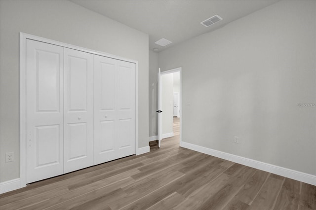 unfurnished bedroom featuring a closet, wood finished floors, visible vents, and baseboards