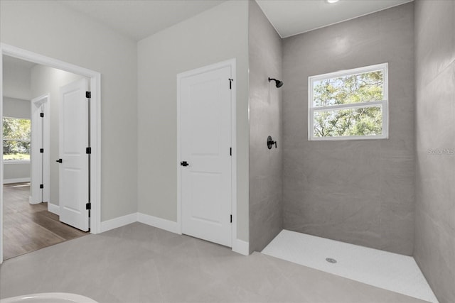 bathroom with a tile shower, a wealth of natural light, and baseboards