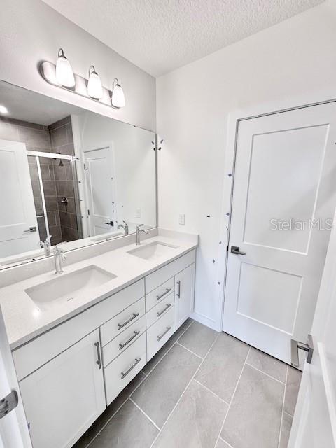 3219 Cup Dr, Lakeland, FL 33803 - bathroom featuring a shower stall, double vanity, a textured ceiling, and tile patterned flooring