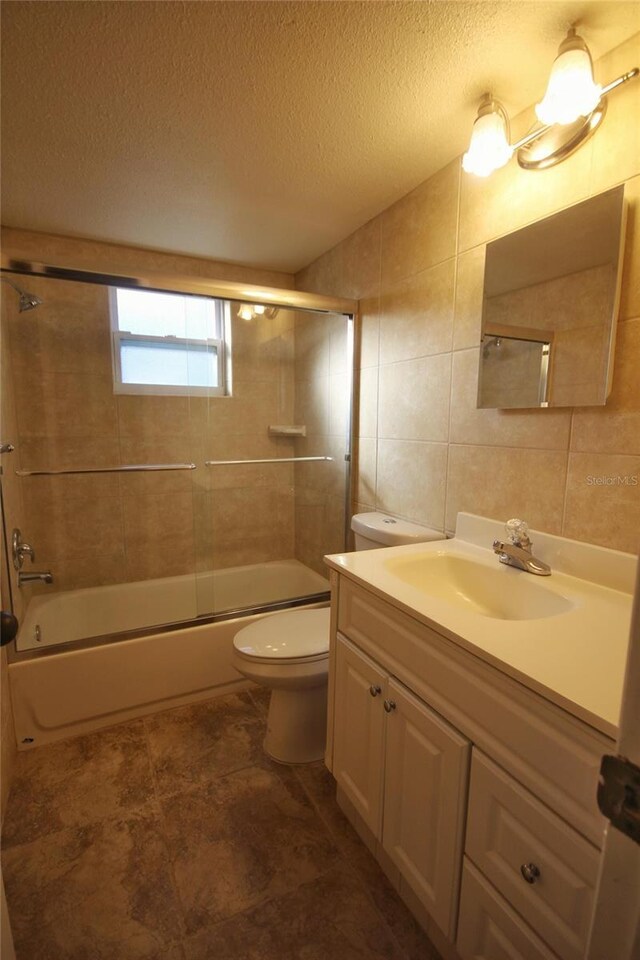 6026 22nd Ave N Unit 4, Saint Petersburg, FL 33710 - full bathroom with tile walls, vanity, combined bath / shower with glass door, a textured ceiling, and toilet
