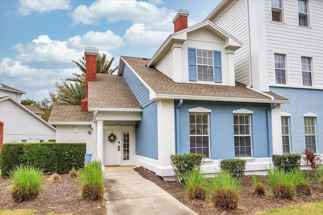 view of front of house featuring roof with shingles, a chimney, and stucco siding