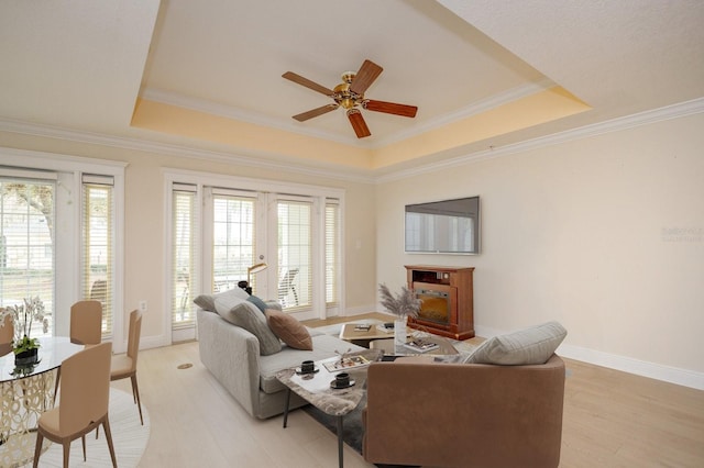 living area featuring light wood-type flooring, ornamental molding, a raised ceiling, and french doors