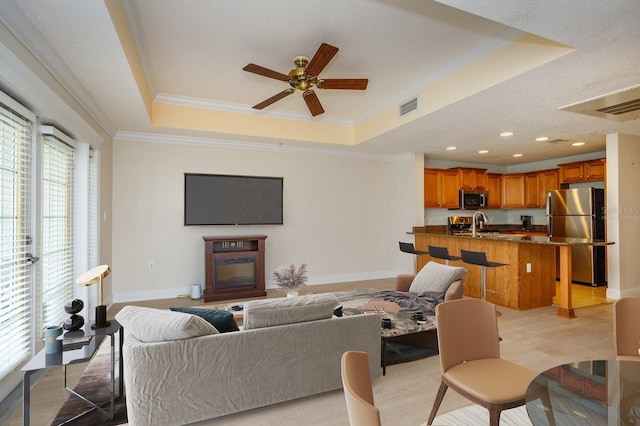 living room featuring ornamental molding, a raised ceiling, visible vents, and baseboards