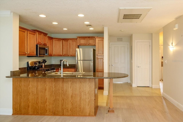 kitchen with appliances with stainless steel finishes, brown cabinetry, a sink, light wood-type flooring, and a peninsula