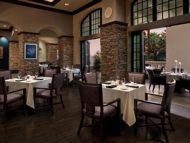 dining area featuring dark wood-style floors, plenty of natural light, decorative columns, and a high ceiling