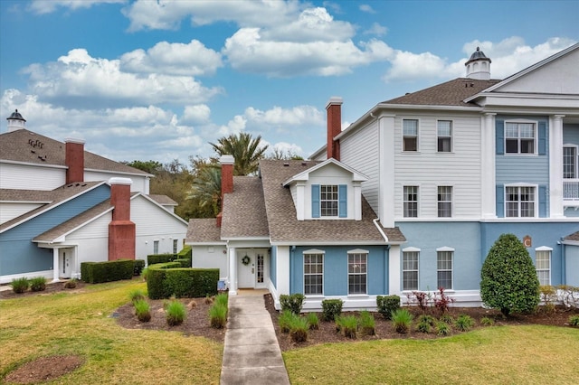 view of front of house with roof with shingles, a front lawn, and a chimney