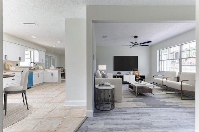 living room featuring light tile patterned flooring, ceiling fan, sink, and a textured ceiling