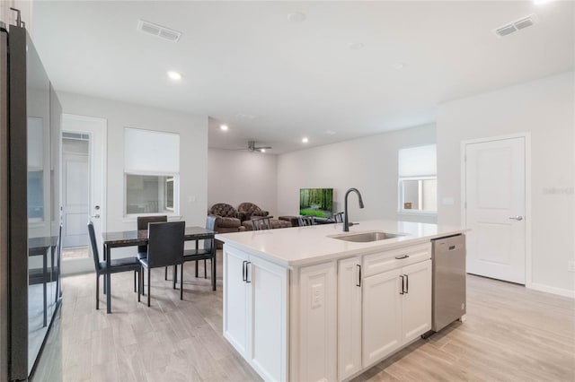 kitchen featuring a sink, white cabinets, light countertops, stainless steel dishwasher, and a center island with sink