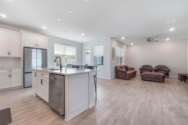 kitchen featuring appliances with stainless steel finishes, open floor plan, a kitchen island with sink, white cabinetry, and a sink