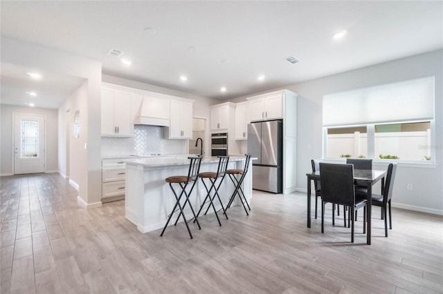 kitchen with stainless steel appliances, white cabinets, light countertops, an island with sink, and a kitchen bar