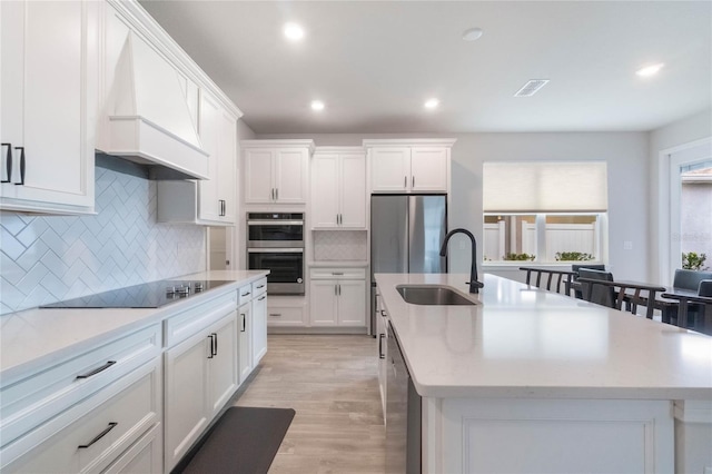 kitchen with an island with sink, premium range hood, appliances with stainless steel finishes, and a sink