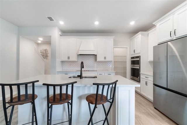 kitchen with a center island with sink, light countertops, appliances with stainless steel finishes, white cabinetry, and a sink