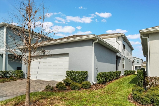 view of side of home featuring decorative driveway, a lawn, an attached garage, and stucco siding