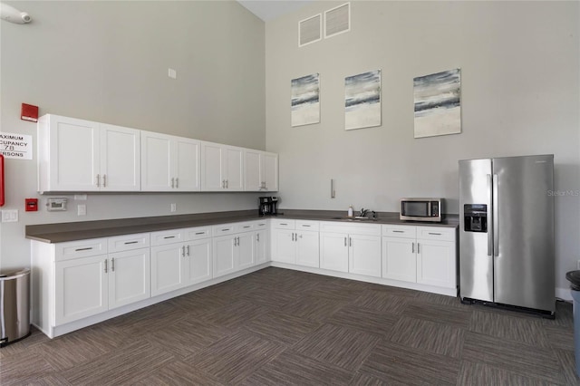 kitchen with stainless steel appliances, dark countertops, visible vents, a towering ceiling, and white cabinets