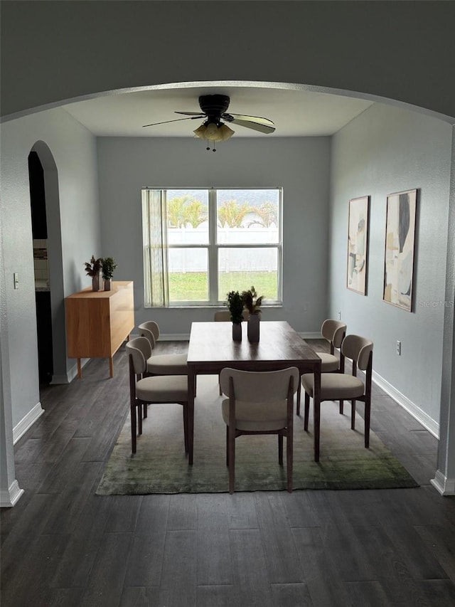 dining room with a ceiling fan, arched walkways, dark wood-style flooring, and baseboards