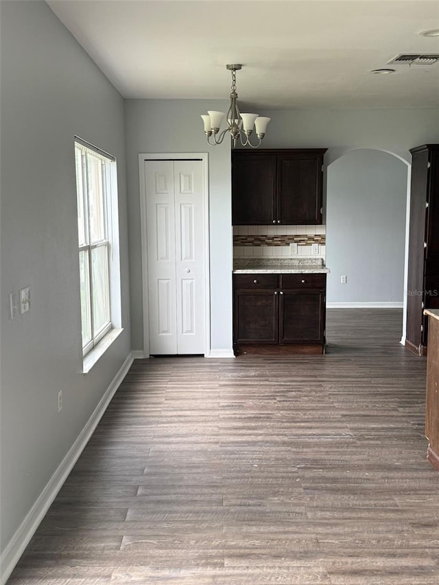 interior space featuring arched walkways, baseboards, wood finished floors, and a notable chandelier