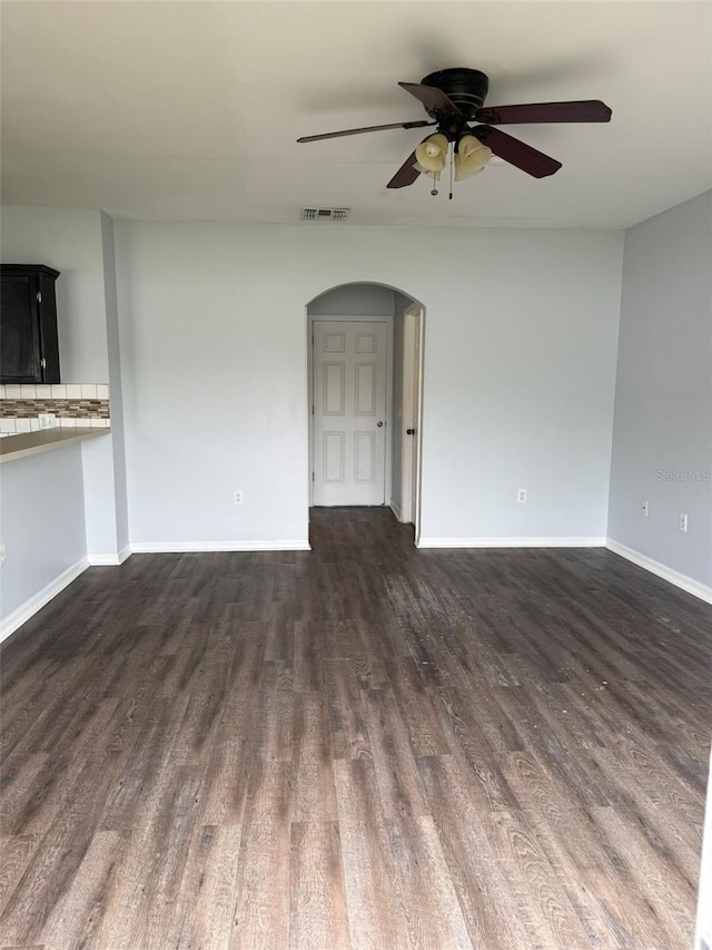 unfurnished living room with baseboards, visible vents, arched walkways, dark wood-style floors, and ceiling fan