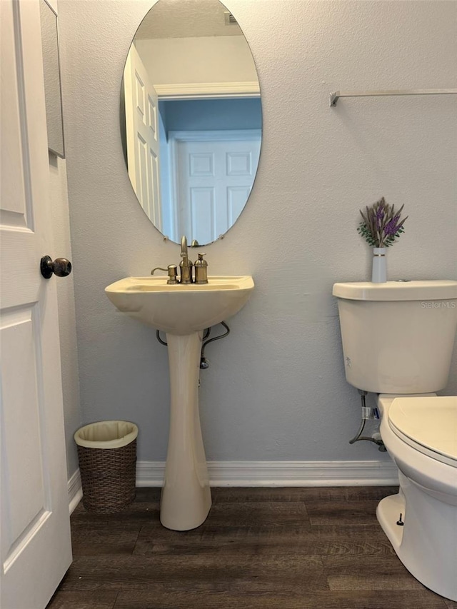 half bathroom with wood finished floors, toilet, and baseboards