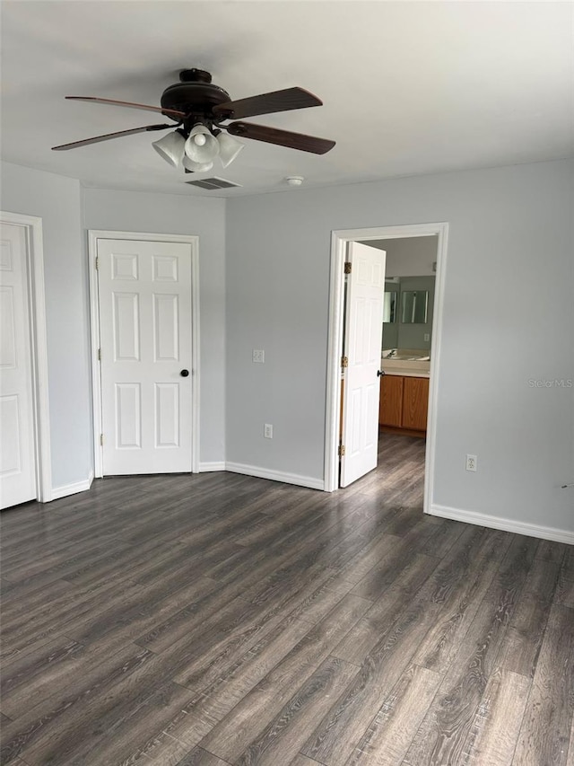 unfurnished bedroom with ensuite bath, ceiling fan, baseboards, and dark wood-type flooring