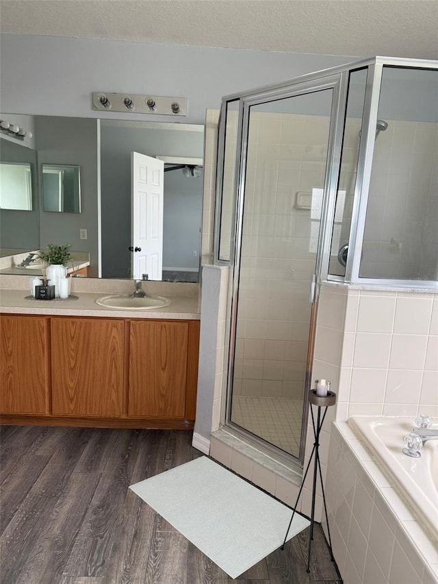 full bathroom featuring a stall shower, vanity, a textured ceiling, wood finished floors, and a bath