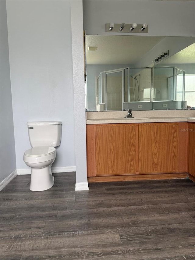 bathroom with wood finished floors, a shower stall, toilet, and baseboards