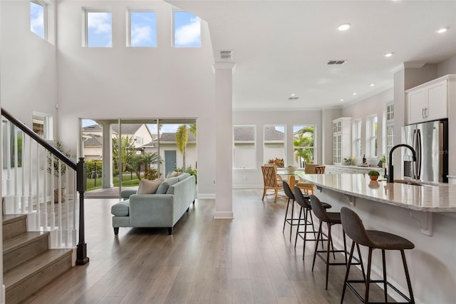 kitchen with stainless steel fridge, light stone counters, a breakfast bar, wood finished floors, and ornate columns