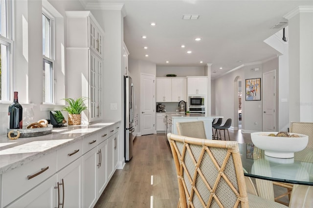 kitchen featuring arched walkways, light wood-style flooring, appliances with stainless steel finishes, ornamental molding, and white cabinets