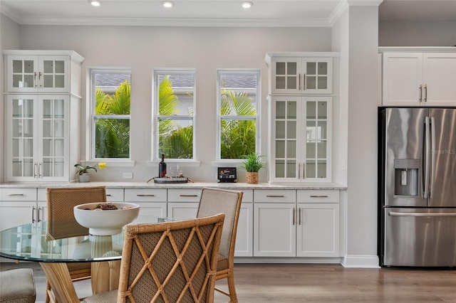 kitchen with a wealth of natural light, white cabinets, stainless steel fridge, and wood finished floors