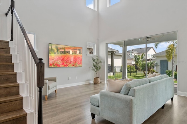 living area with stairs, a towering ceiling, baseboards, and wood finished floors