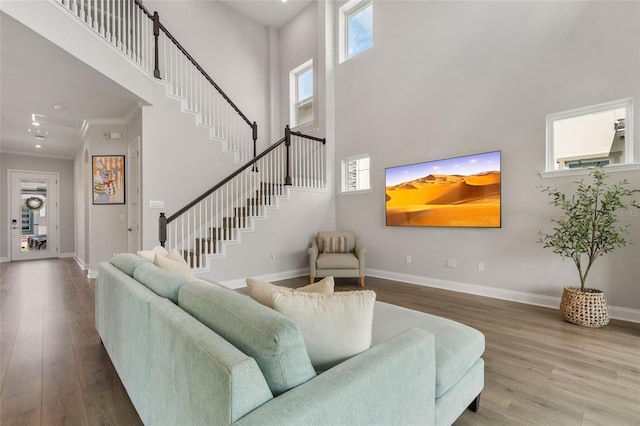 living area with crown molding, stairway, baseboards, and wood finished floors