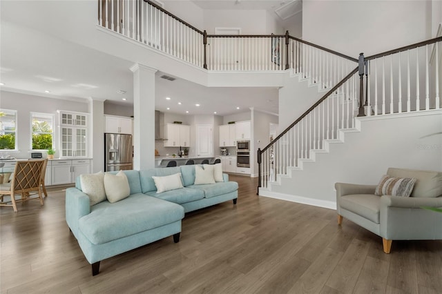 living area with recessed lighting, a high ceiling, wood finished floors, baseboards, and stairway