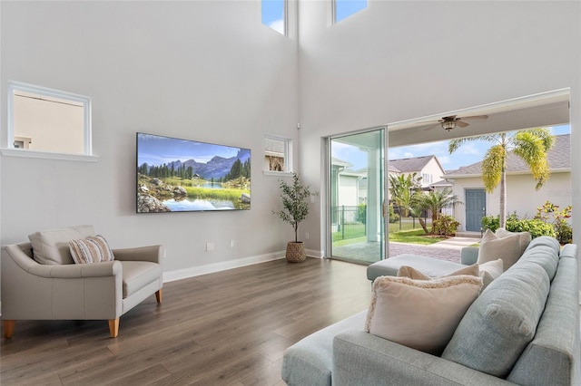 living area with a ceiling fan, a high ceiling, baseboards, and wood finished floors