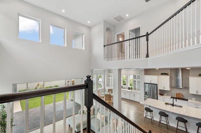 corridor featuring light wood-style flooring, a high ceiling, an upstairs landing, a sink, and recessed lighting