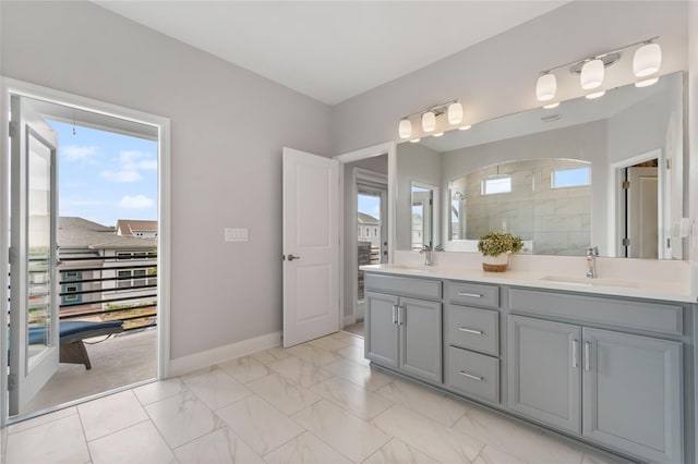 full bathroom featuring a sink, baseboards, marble finish floor, tiled shower, and double vanity