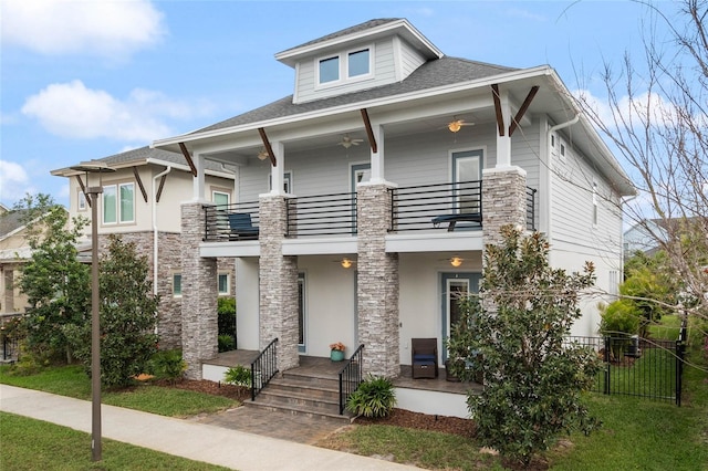 view of front of house with stone siding, ceiling fan, a balcony, and fence