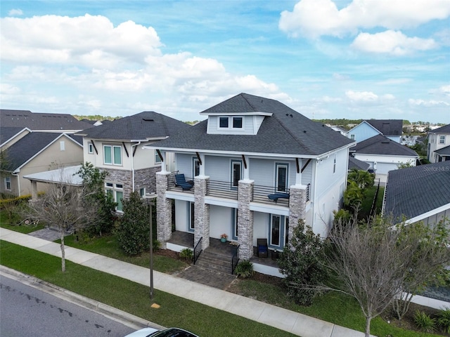 view of front of property featuring central air condition unit, a shingled roof, a balcony, a residential view, and stone siding