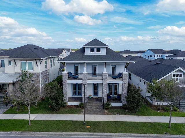 view of front of home with a residential view, roof with shingles, a balcony, and a front yard