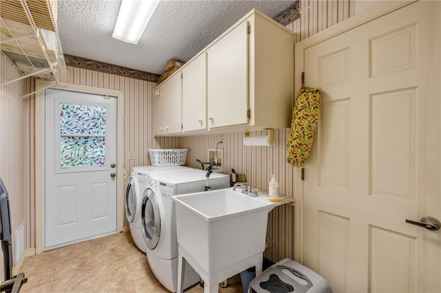 clothes washing area featuring washing machine and clothes dryer, a textured ceiling, light tile patterned floors, sink, and cabinets