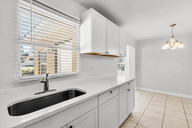 kitchen with light tile patterned floors, hanging light fixtures, white cabinetry, a sink, and baseboards