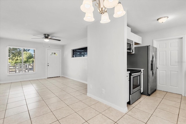 kitchen with light tile patterned floors, ceiling fan with notable chandelier, stainless steel appliances, baseboards, and white cabinets