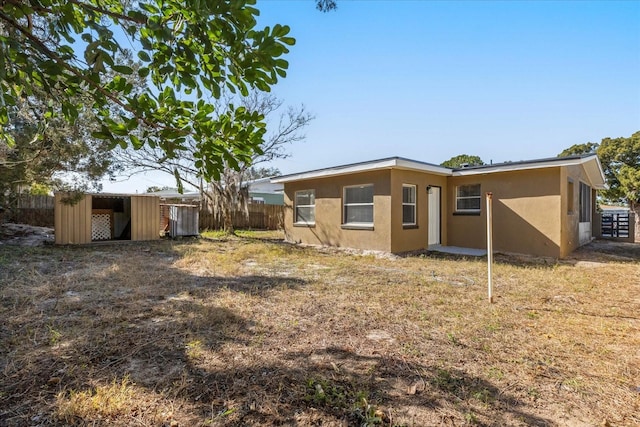 rear view of property featuring an outdoor structure, fence, and stucco siding