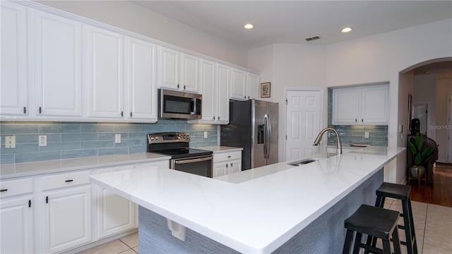 kitchen with light tile patterned flooring, white cabinetry, stainless steel appliances, an island with sink, and a breakfast bar area