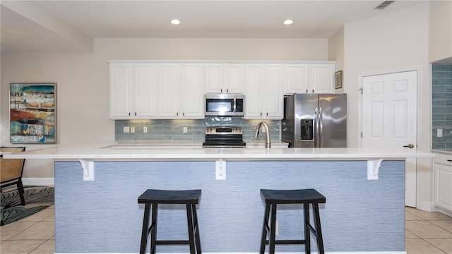 kitchen with light tile patterned floors, stainless steel appliances, white cabinetry, and a breakfast bar